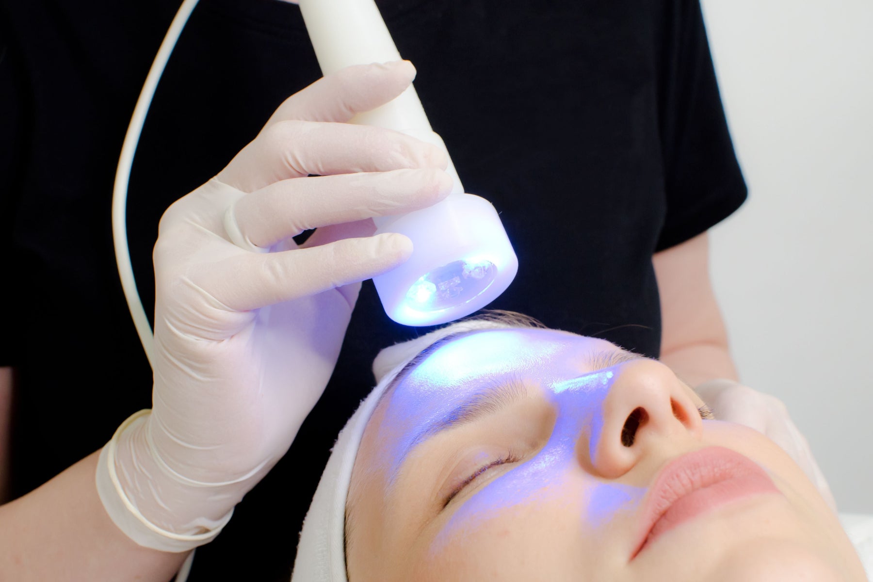 Beauty therapist using blue light tool on client